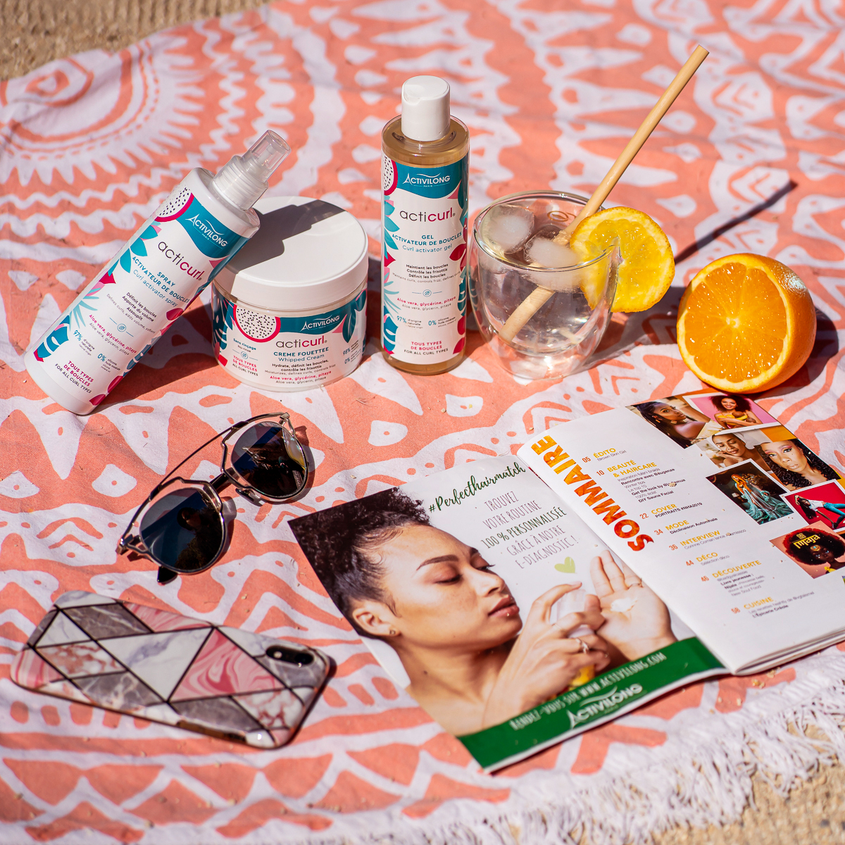 Produits capillaires, lunettes de soleil, smartphone, verre d'eau glacée et prospectus sur une serviette de plage